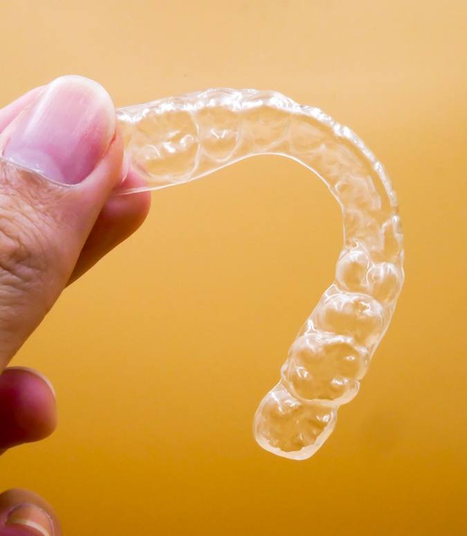 Close up of woman holding a clear aligner with yellow background