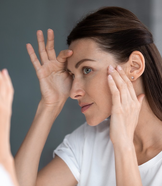 Woman looking in mirror, concerned about the appearance of wrinkles