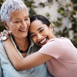 Mother and daughter smiling and hugging outside