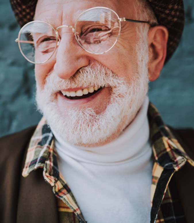 Senior man with glasses smiling in front of wall