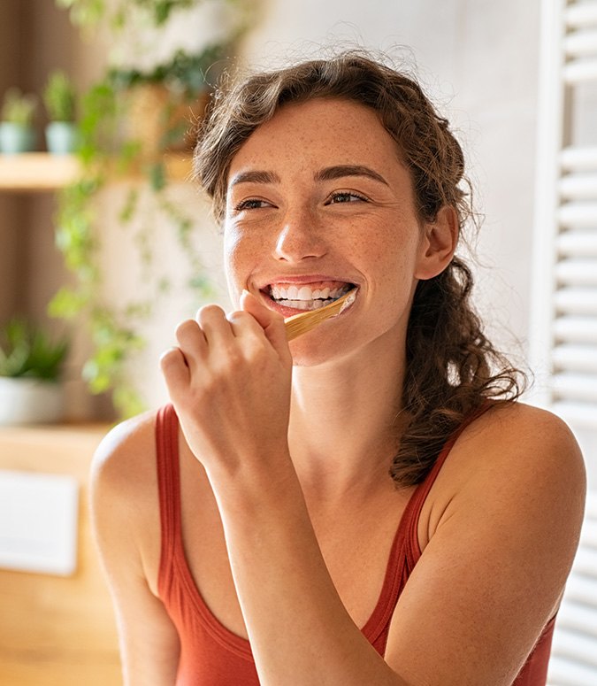 A woman brushing her teeth in front of a bathroom mirror